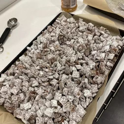 A bowl of homemade Muddy Buddies coated with powdered sugar, perfect for parties and snacks.