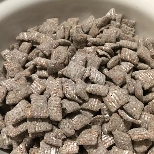 A bowl of homemade Muddy Buddies coated with powdered sugar, perfect for parties and snacks.