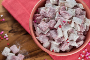 A bowl of homemade Muddy Buddies coated with powdered sugar, perfect for parties and snacks.