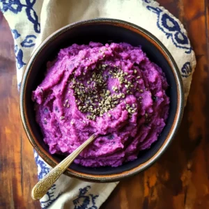 Vibrant purple sweet potato mash garnished with fresh herbs, served in a white bowl on a rustic wooden table.